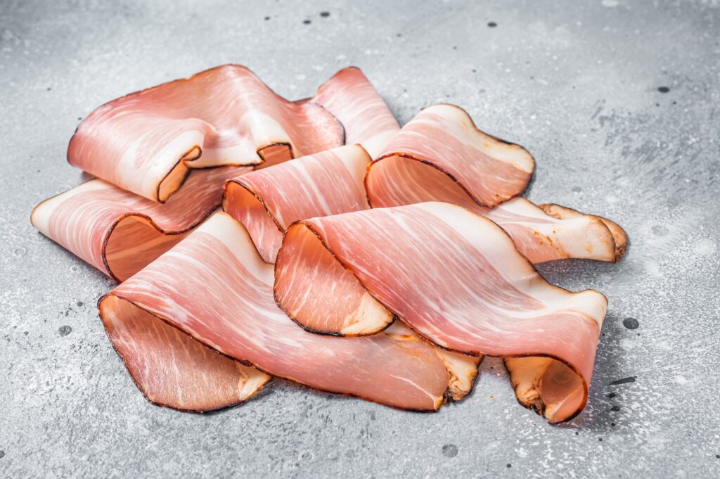 Black Forest Ham Slices on kitchen table. Gray background. Top view